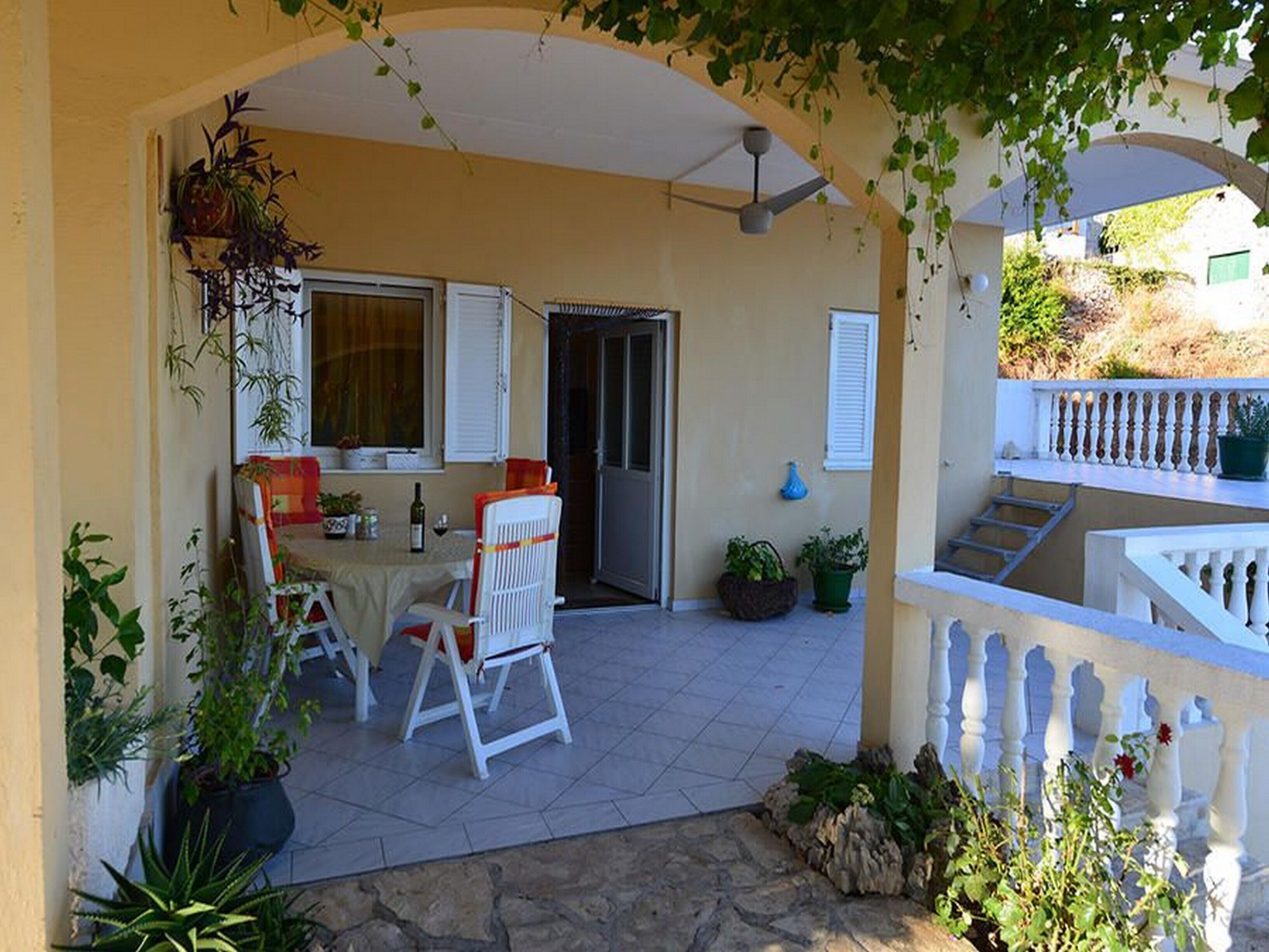 Un espacio al aire libre con patio, una mesa, sillas, un ventilador de techo y plantas en macetas.