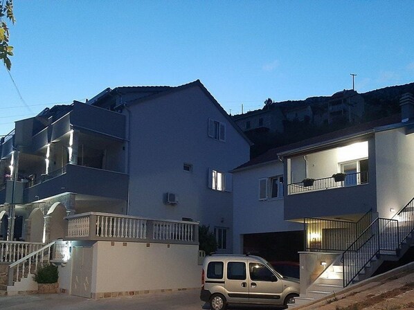 A multi-story residential building with balconies, a garage, and a van parked in front.