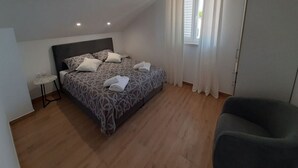 Ett sovrum med en säng, en stol, ett litet bord och ett fönster med gardiner.