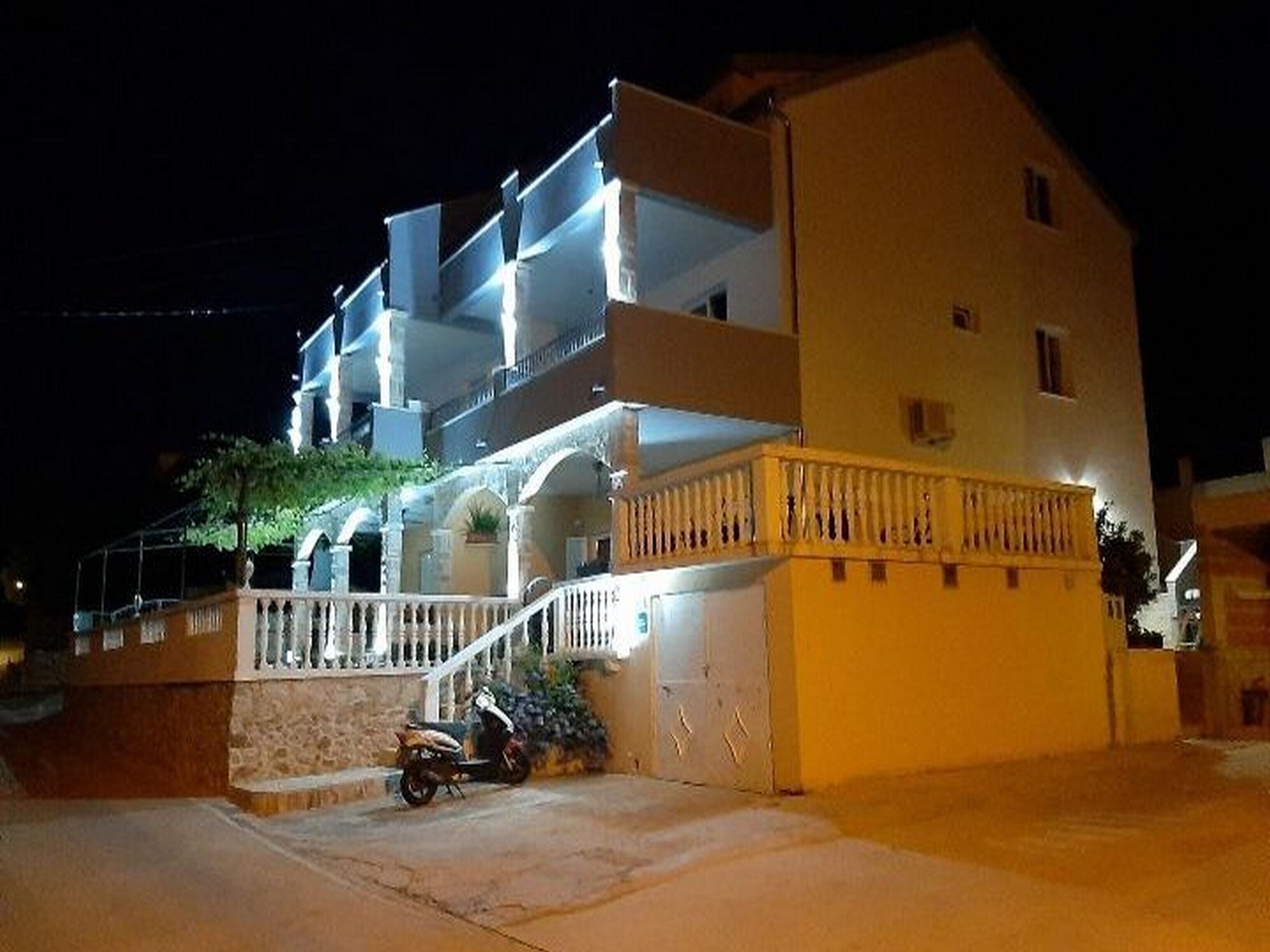 A multi-story hotel with a balcony on the second floor, a staircase leading to the entrance, and a parked motorcycle in front.