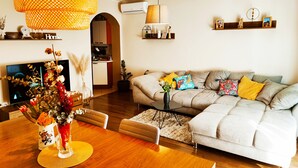 Un soggiorno moderno con un divano, un tavolo da pranzo con sedie, una TV e un'area cucina sullo sfondo.