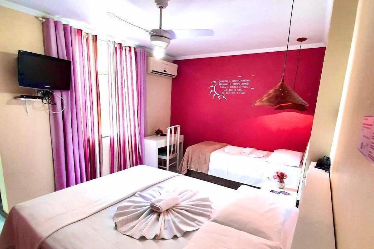 Una habitación de hotel con dos camas, un televisor de pantalla plana montado en la pared y un ventilador de techo.