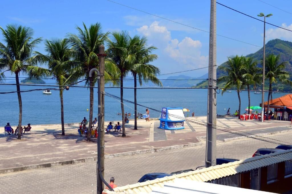 Vista de la playa con palmeras, un pequeño quiosco y una carretera con coches estacionados.