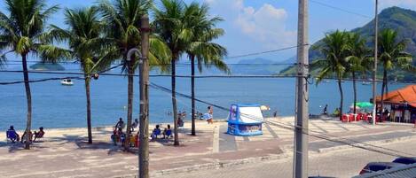 Vista de la playa con palmeras, un pequeño quiosco y una carretera con coches estacionados.