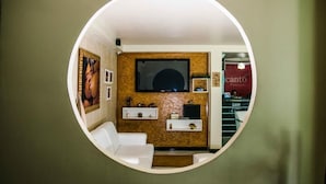 Vista circular de una habitación con televisión montada en la pared, un sofá blanco y una mesita con objetos decorativos.