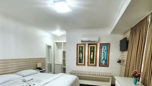 Habitación de hotel con una cama grande, un escritorio y una silla. Hay un televisor en la pared y una ventana con cortinas.