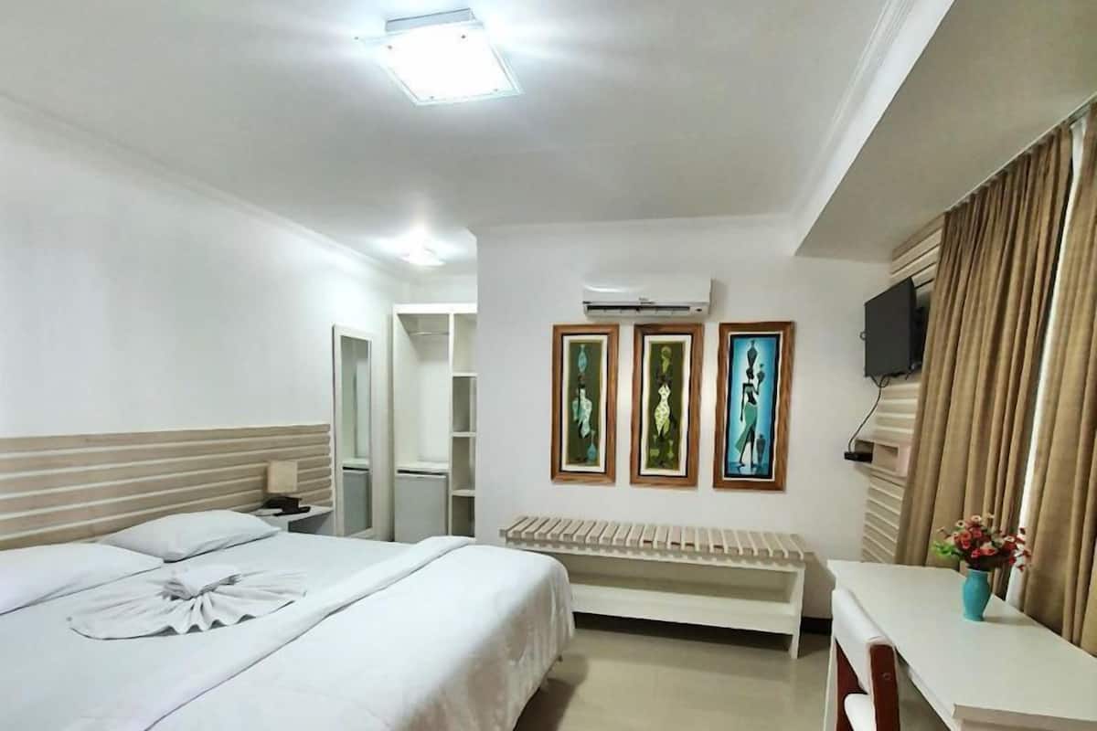 Habitación de hotel con una cama grande, un escritorio y una silla. Hay un televisor en la pared y una ventana con cortinas.