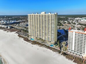 A high-rise hotel with multiple balconies, a swimming pool, and a beach view.
