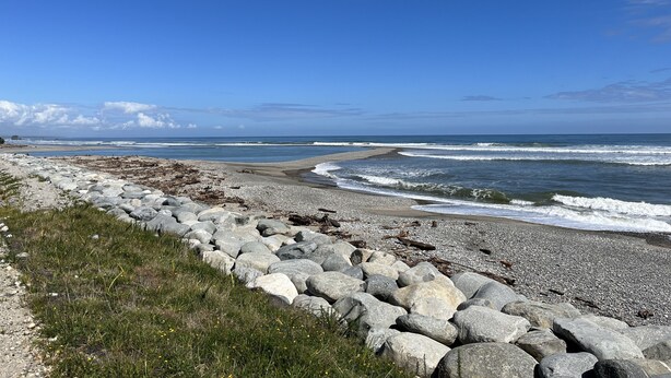Een rotsachtig strand met golven die op de kust breken, onder een heldere blauwe lucht.