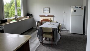Een keuken met een eettafel, een koelkast en een raam met uitzicht op groen.
