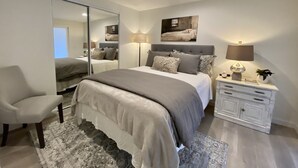 Une chambre à coucher comprenant un lit, une chaise, une table de chevet, un miroir et une lampe fixée au mur.
