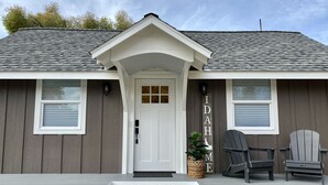 Une maison avec un porche à l’avant, une porte blanche, deux fenêtres avec volets et une enseigne sur laquelle on peut lire « IDAHO HOME ».