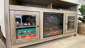 Un meuble en bois doté de portes en verre, contenant des jeux de société et une cheminée.
