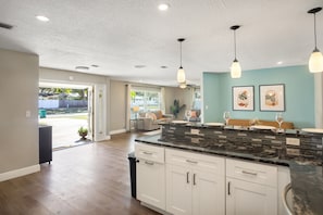 A modern kitchen with white cabinets, a granite countertop, pendant lighting, and a view to the backyard. - Lovely Pool Home, Close to beaches! Antilles (Largo)