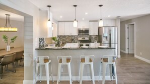 Una cocina moderna con una isla central, taburetes de bar, iluminación colgante y electrodomésticos de acero inoxidable.