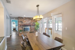 A dining area with a wooden table, chairs, a hanging light fixture, a brick fireplace, and a view through large windows. - Lovely Pool Home, Close to beaches! Antilles (Largo)