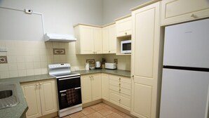 Una cocina con gabinetes blancos, estufa, microondas y refrigerador.