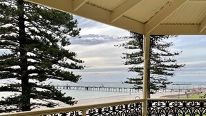 Un espace extérieur abrité doté d’une terrasse en bois, d’une rambarde en métal et offrant une vue sur la mer et un quai.