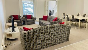 Una sala de estar con sofás estampados, una mesa de comedor con sillas y un televisor sobre un mueble.