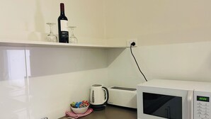 Una cocina con microondas, tostadora, hervidor y una botella de vino en un estante.