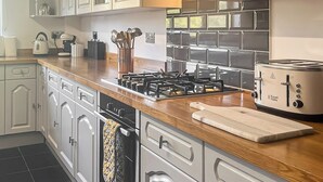A modern kitchen with white cabinetry, a wooden countertop, a gas stove, a toaster, and a cutting board. - 3 bedroom accommodation in Johnston, near Haverfordwest (Johnston, near Haverfordwest)