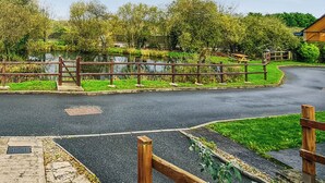A park with a paved walkway, a wooden fence, and a pond. - 3 bedroom accommodation in Johnston, near Haverfordwest (Johnston, near Haverfordwest)