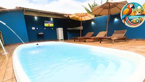 Une piscine avec des chaises longues et des parasols, un écran de télévision et un mur bleu.