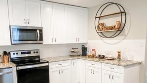 Une cuisine moderne avec des armoires blanches, des appareils en acier inoxydable, un plancher en bois et un panneau décoratif portant l’inscription « Cheer » au mur.