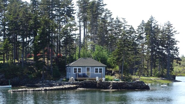 Ett litet hus med en brygga, omgivet av tät skog och en stilla sjö.