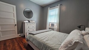 Une chambre à coucher comprenant un lit, une commode, un miroir, une fenêtre avec des stores et une porte.
