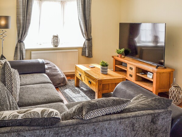 A living room with a sofa, a coffee table, a TV on a wooden stand, and a window with curtains.