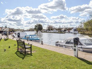 A riverside area with boats docked, a bench, and a grassy area with pigeons.