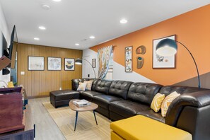 A modern living room with a leather sofa, a wooden accent wall, and a large window with curtains.