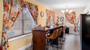 A dining area with a wooden table, chairs, and a window with floral curtains. - 5 mins to DT, family friendly, hot tub, arcade, sleeps 8, fully fenced yard. (Chattanooga)