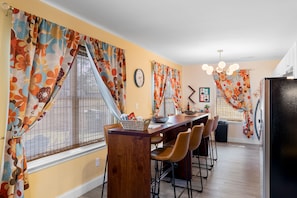 A dining area with a wooden table, chairs, and a window with floral curtains.