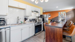 A modern kitchen with white cabinets, stainless steel appliances, and a wooden island with bar stools. - 5 mins to DT, family friendly, hot tub, arcade, sleeps 8, fully fenced yard. (Chattanooga)