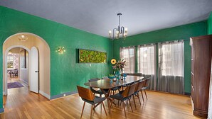 Un comedor con mesa y sillas de madera, una araña y una pared verde.