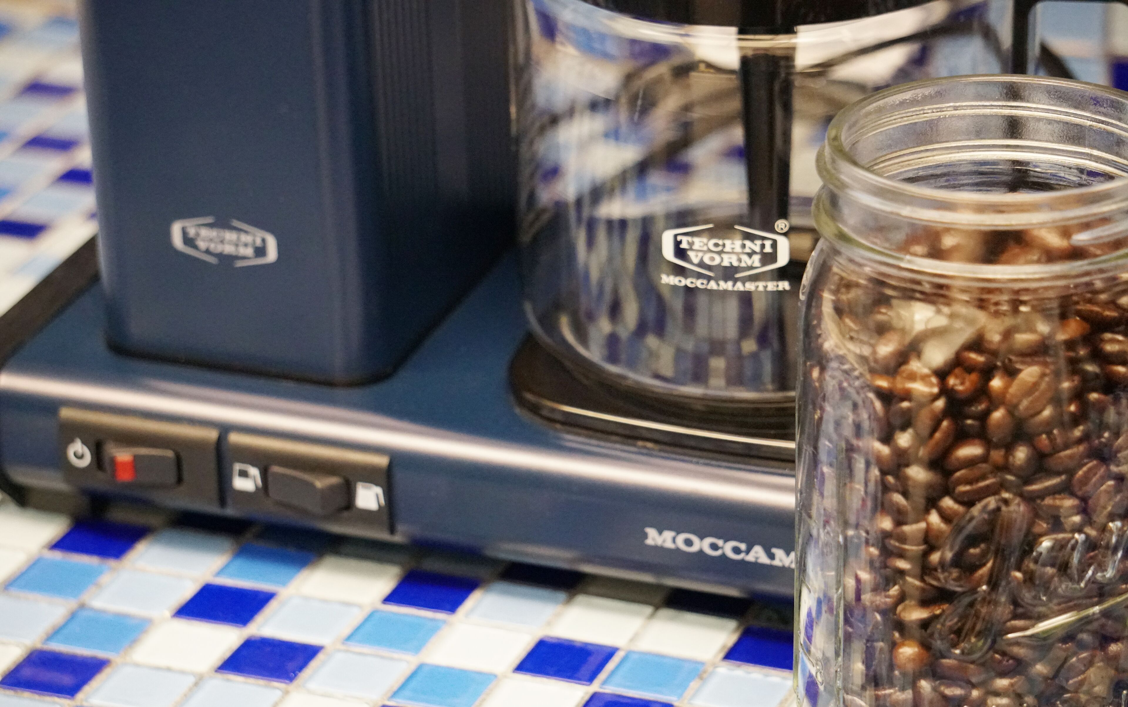 Une machine à café et un bocal de grains de café sur une surface carrelée.