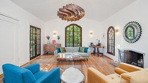 Una sala de estar amplia con piso de madera, un sofá estampado, un sillón azul, una mesa de centro redonda y una chimenea.