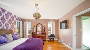Un dormitorio con una cama grande, cómoda, tocador y televisor en la pared.