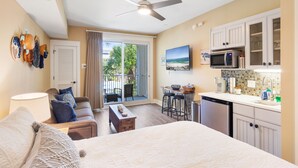 A compact hotel room with a balcony, a kitchenette, and a bed.