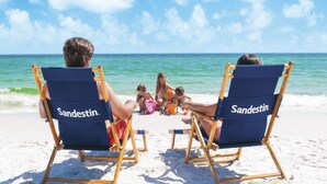 Two beach chairs with the brand name 'Sandestin' on the backrests, facing the ocean.