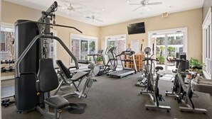 A gym with various exercise equipment, ceiling fans, and large windows.