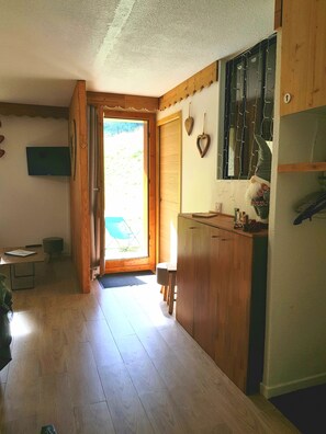 A cozy kitchen with wooden cabinets, a small countertop, and a door leading to a bright outdoor area. - Valmorel - Beautiful Apartment at the Foot of the Slopes (Les Avanchers-Valmorel)
