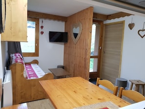 A cozy room with a wooden table, a bed with a pink and white bedspread, a TV mounted on the wall, and a wooden door with heart decorations. - Valmorel - Beautiful Apartment at the Foot of the Slopes (Les Avanchers-Valmorel)
