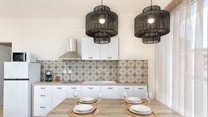Une cuisine moderne avec des meubles blancs, une table à manger en bois pour quatre personnes et deux suspensions noires.