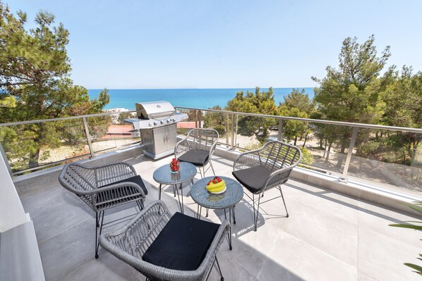A balcony with wicker furniture, a grill, and a view of the sea.