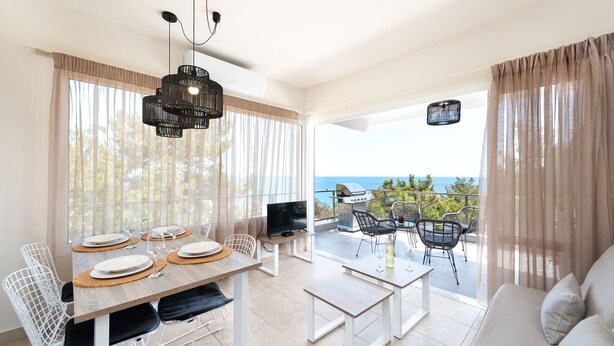 Un coin repas avec une table dressée pour quatre personnes, un téléviseur et un barbecue à l’extérieur.