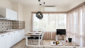 Une cuisine moderne avec des meubles blancs, une table à manger pour quatre personnes, un téléviseur et un canapé dans l’espace salon.