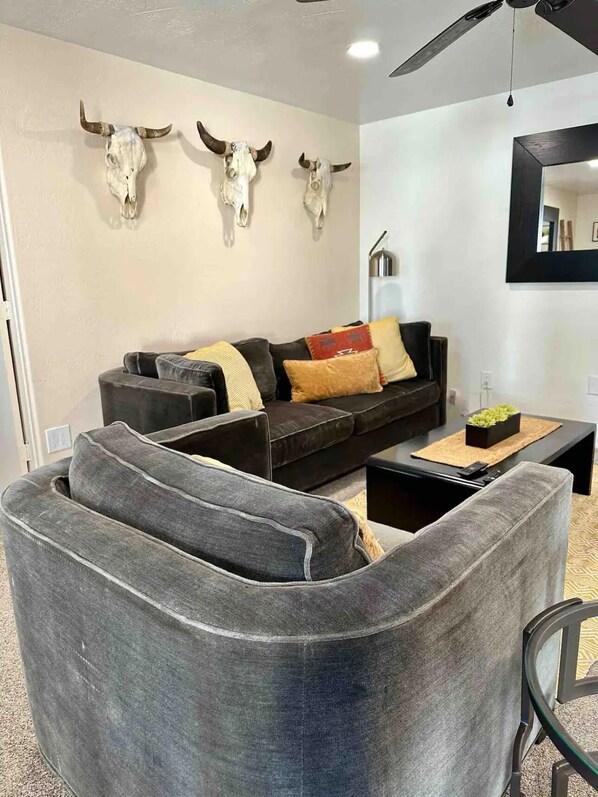 A living room with a grey sofa, a coffee table, and three mounted cow skulls on the wall. - Pro Putting Green, Spa, Pool, Outdoor Kitchen (Chandler)